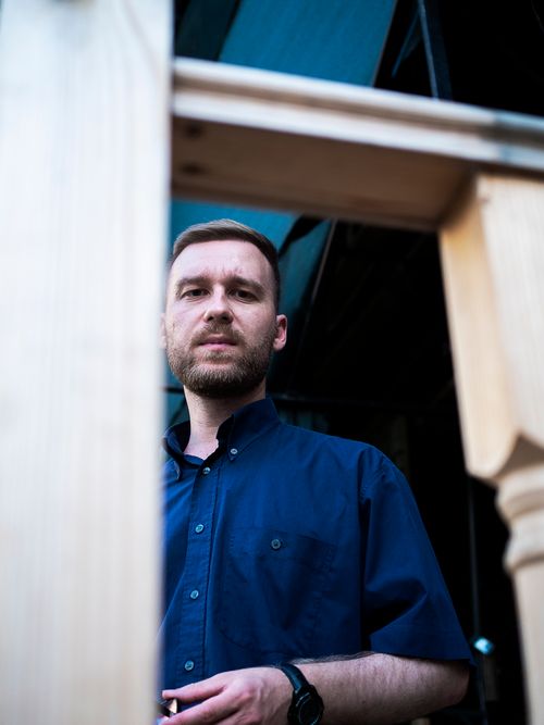 Free Serious man in blue shirt outdoors, framed by wooden structure. Urban portrait. Stock Photo