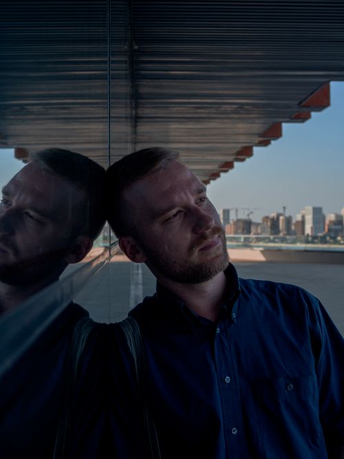 Free Portrait of a man leaning on a reflective wall with a city skyline in the background. Stock Photo