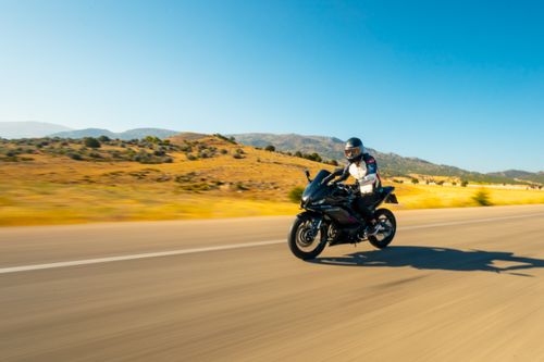 Free Motorcyclist riding fast on a wide, open desert road under a bright blue sky. Stock Photo