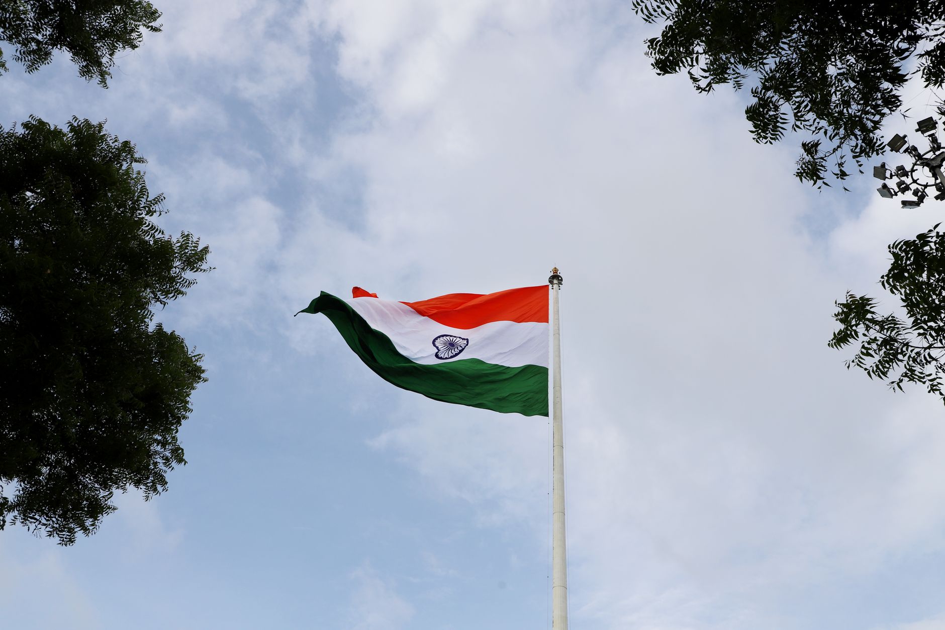 Low angle shot of the Indian national flag on a flagpole with a clear blue sky.