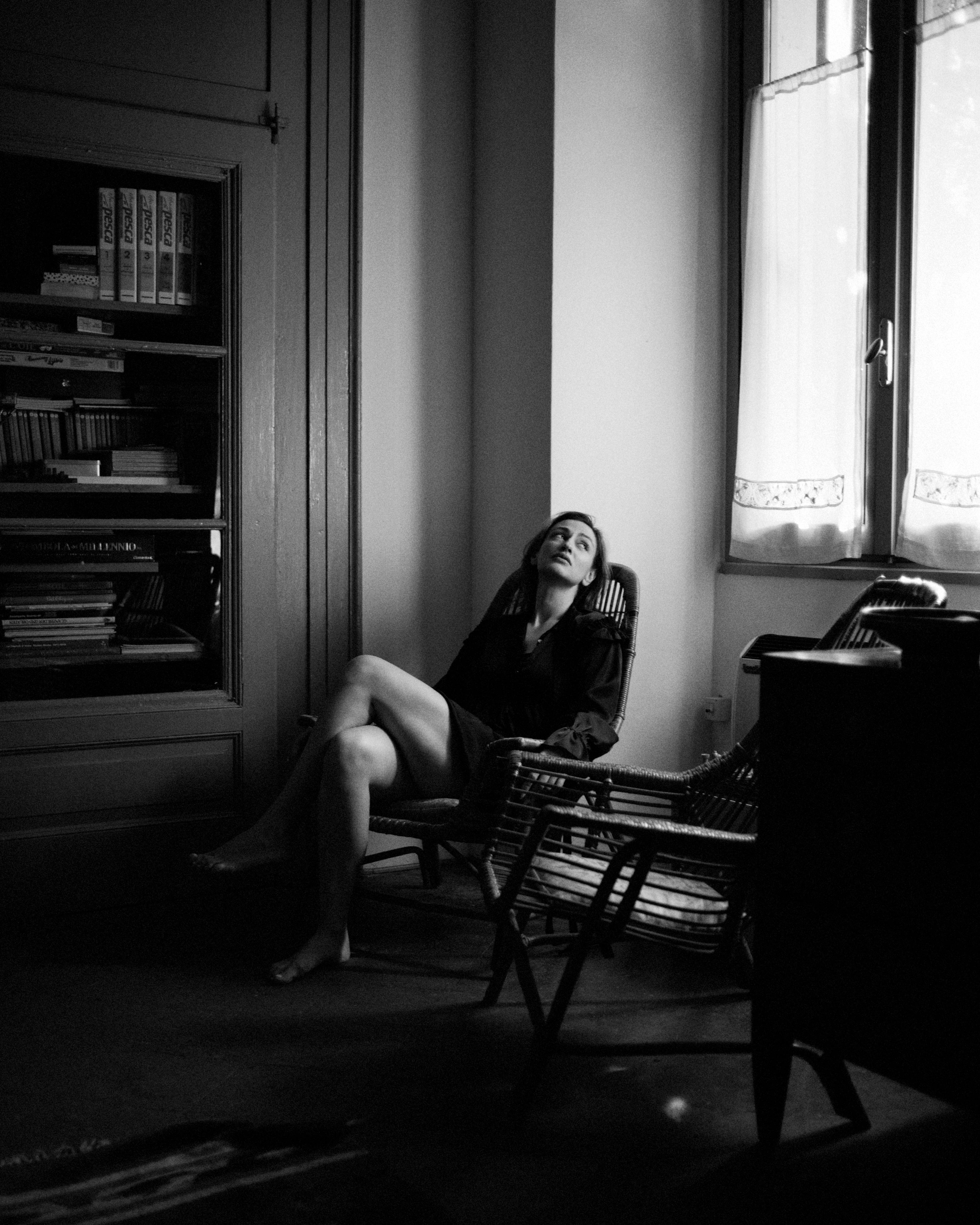 woman in black dress sitting in wooden rocking chair looking towards window