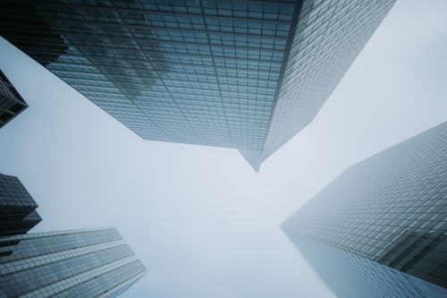 Free Low angle view of modern glass skyscrapers disappearing into the foggy sky, creating a dramatic urban scene. Stock Photo