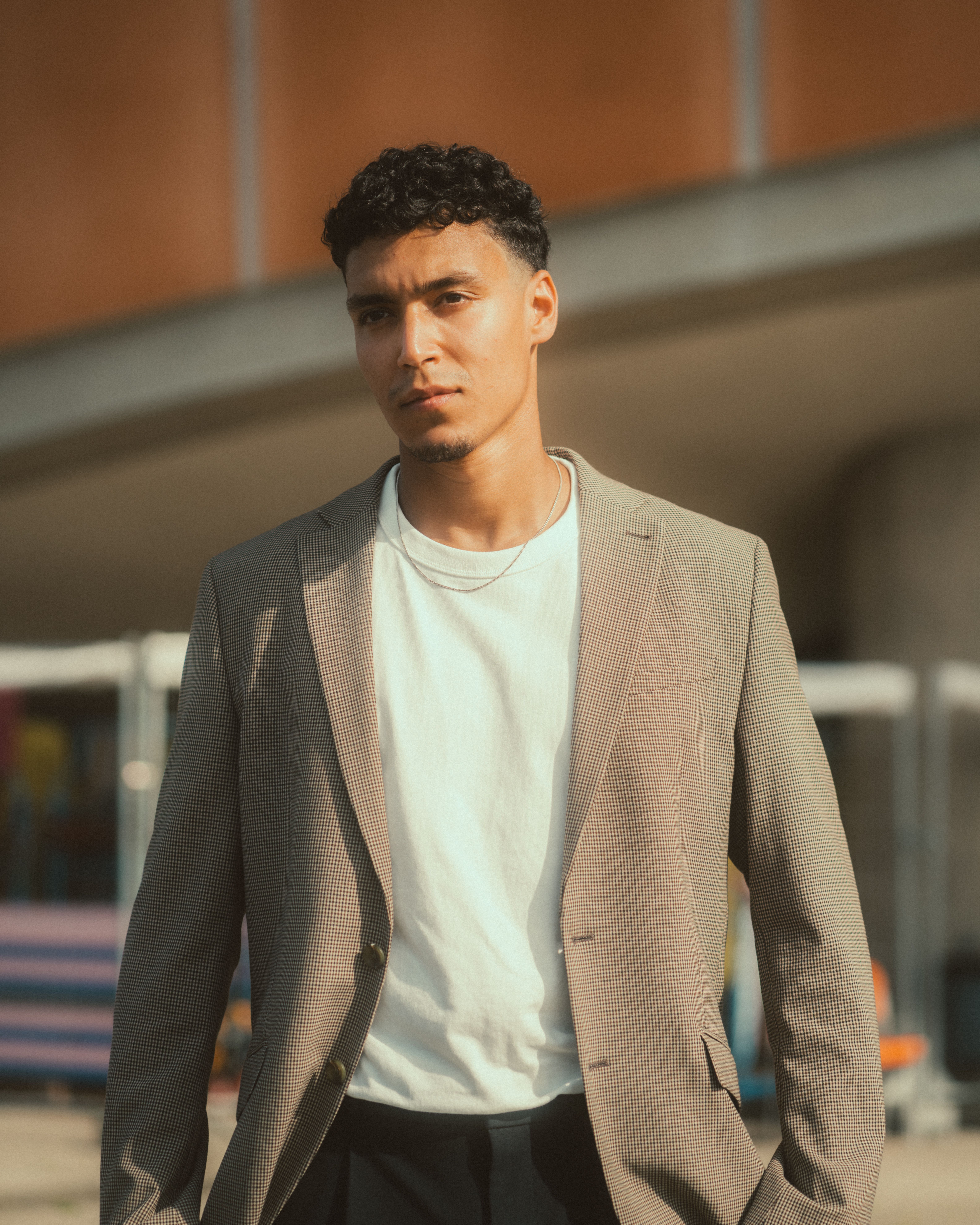 Fashion portrait of a man in a beige jacket and white t-shirt posing outdoors in Berlin.