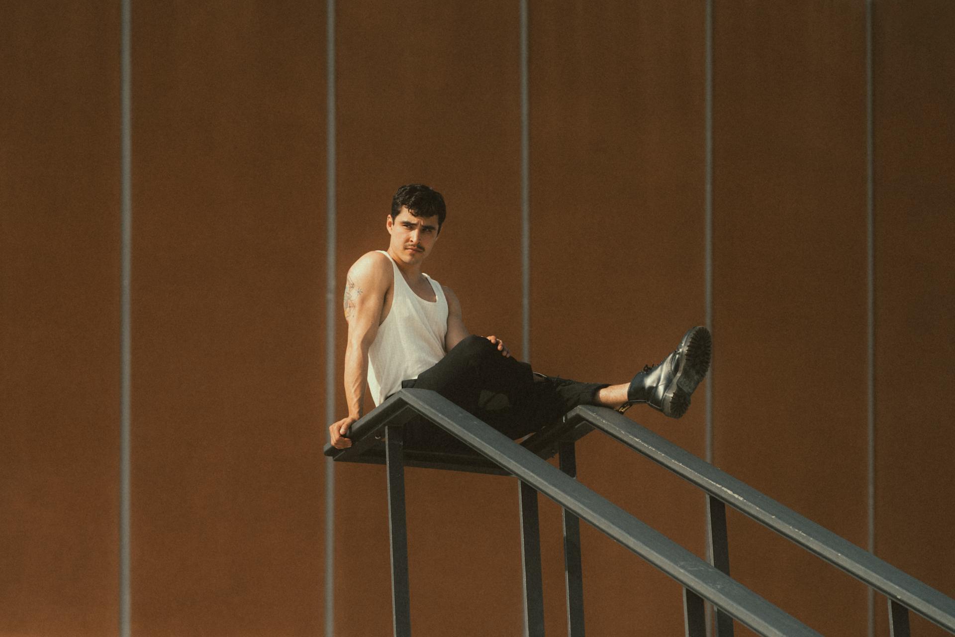 Muscular Man Wearing Tank Top Sitting on Staircase Railing Outdoors