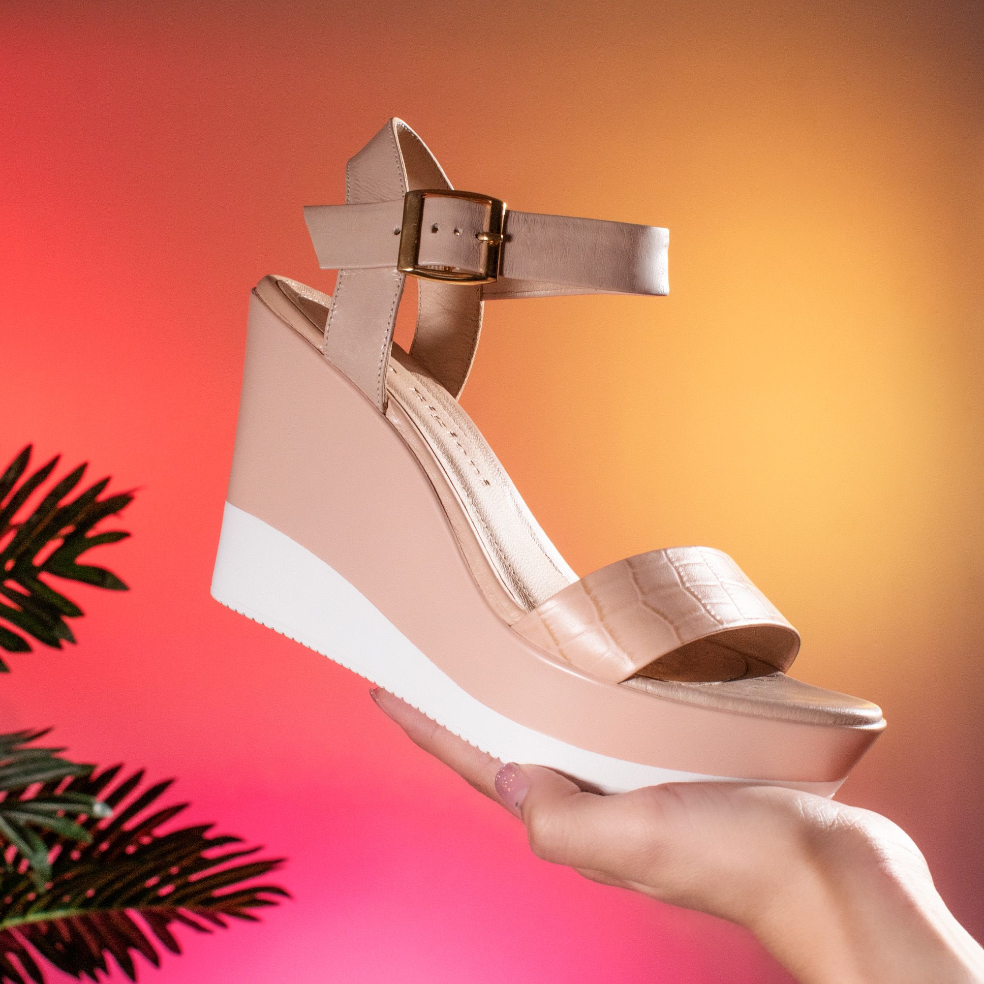 Stylish beige wedge sandal held against a vibrant gradient backdrop. Perfect for fashion shoots.