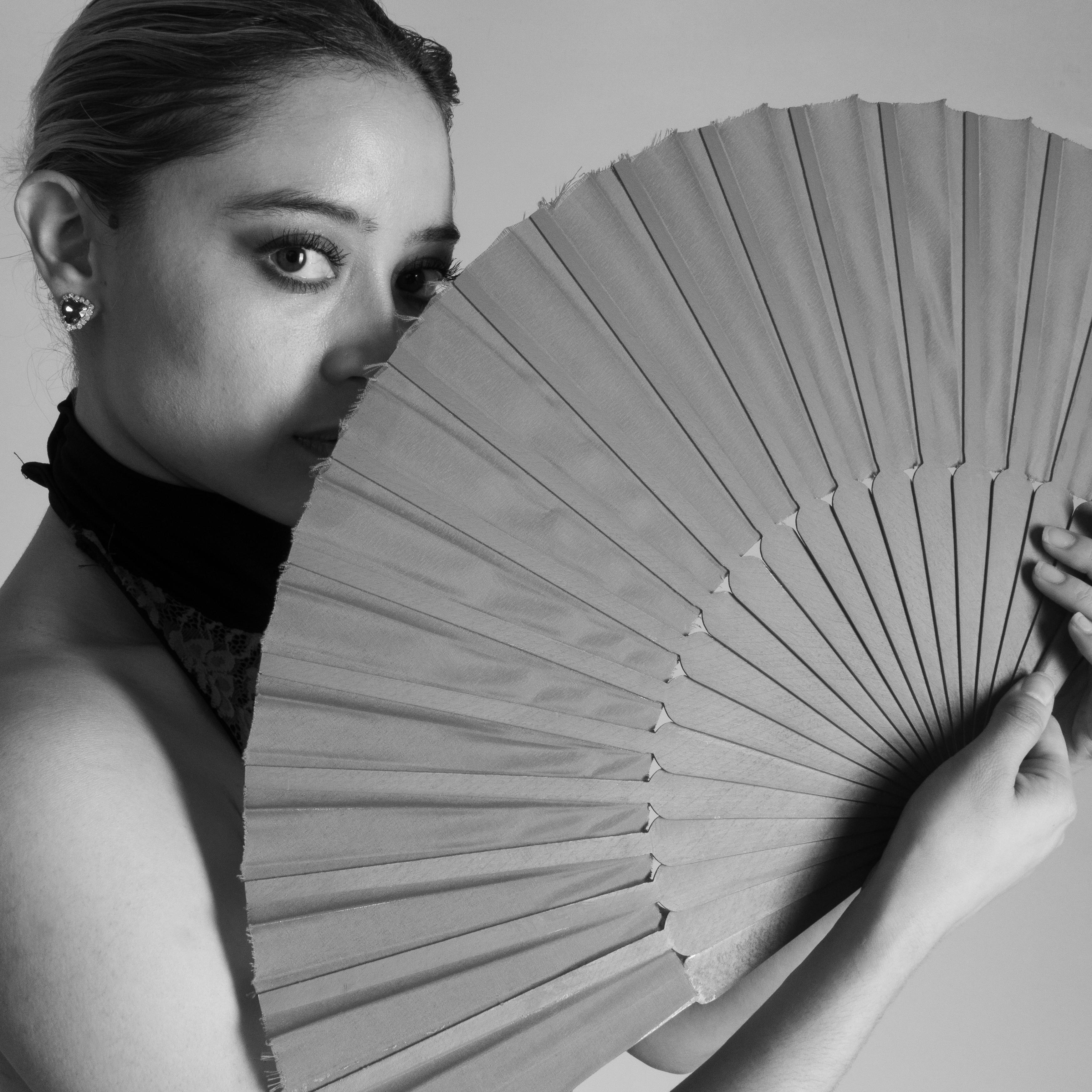 Black and white portrait of a woman holding a fan, showcasing elegance and mystery.