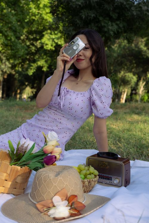 Free Woman sitting in a park, holding a camera with a picnic setup. Vintage vibes. Stock Photo