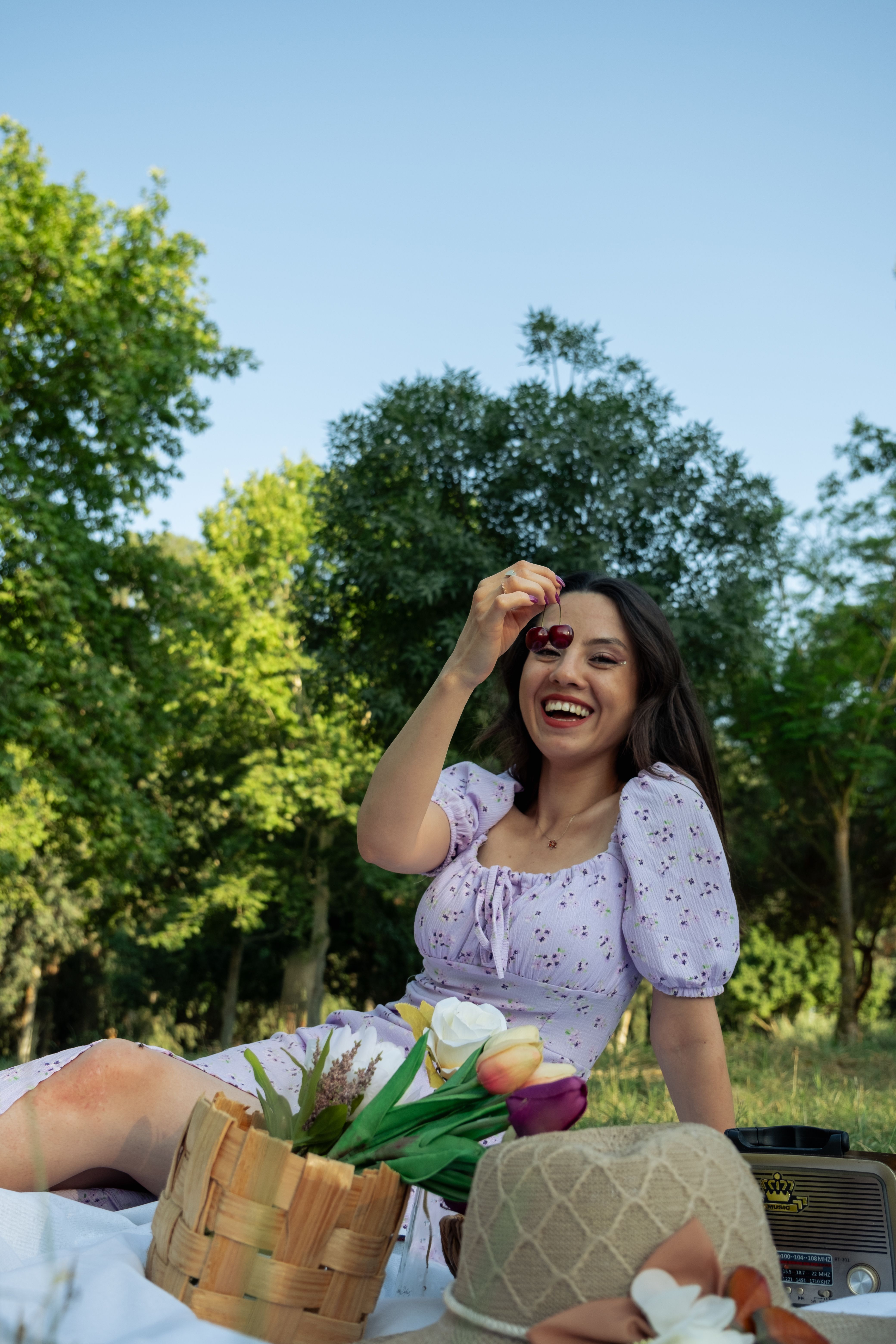 Smiling woman enjoys a picnic in the park, holding a cherry playfully.