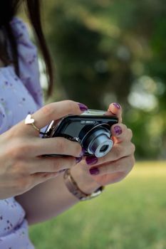 Close-up of a woman with purple nails holding a digital camera outdoors, capturing nature.