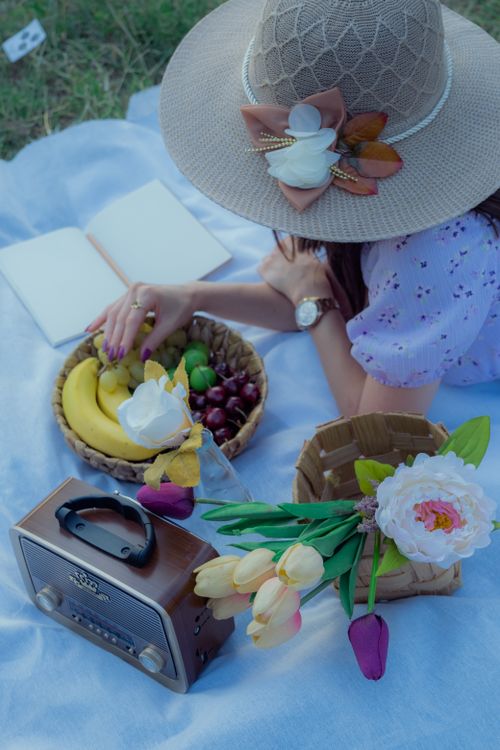 Free A serene spring picnic featuring a woman with tulips, fruits, and a vintage radio. Stock Photo
