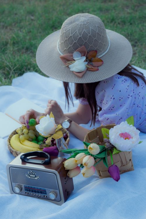 Free A woman relaxing on a picnic outdoors with fruits, flowers, and a vintage radio. Stock Photo