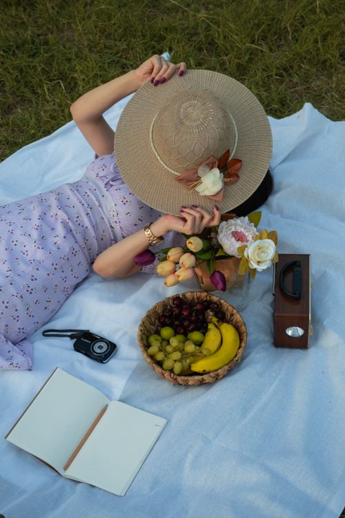 Free Woman enjoying a relaxing summer picnic in a field with fruits, flowers, and a vintage radio. Stock Photo