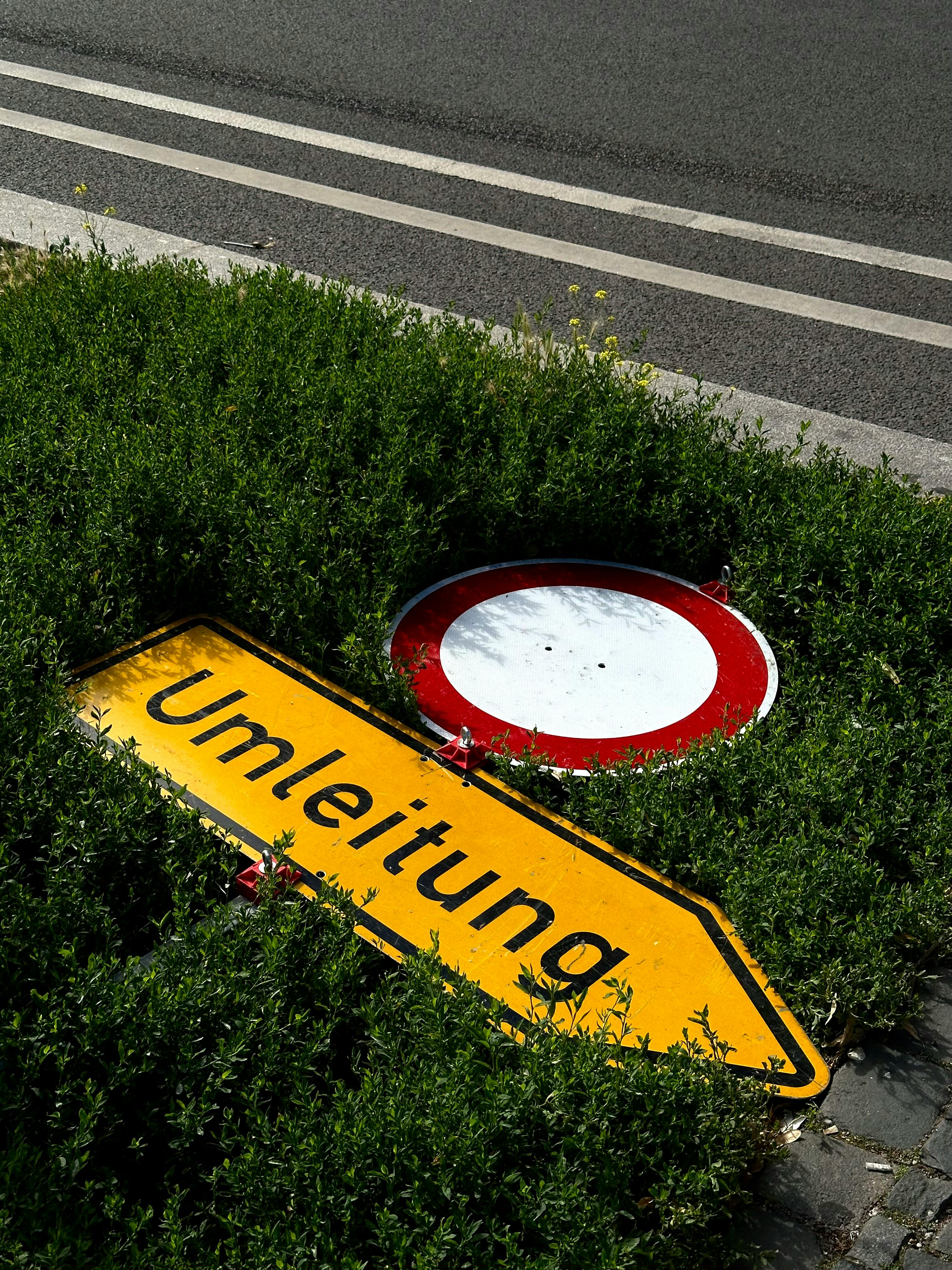 Fallen yellow 'Umleitung' sign surrounded by green grass in Berlin.