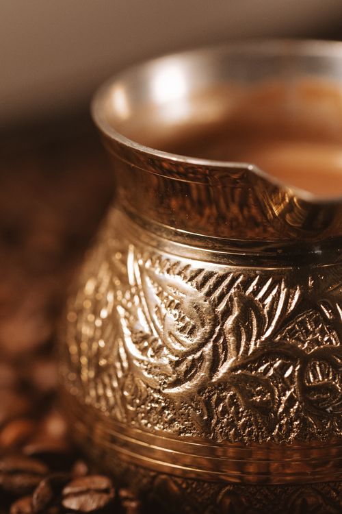 Free Close-up of an ornate bronze coffee pot amidst scattered coffee beans, highlighting craftsmanship. Stock Photo