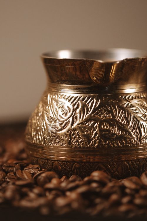 Free A detailed bronze coffee pot sits among coffee beans, capturing its vintage charm. Stock Photo