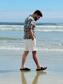 Man strolling on Tofino's shore in summer attire, capturing a peaceful beach moment.