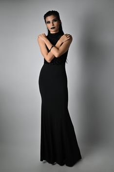 Stylish woman in black dress posing with elegance against gray background.