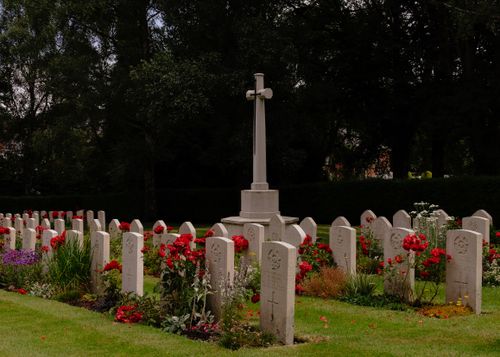 Free Peaceful cemetery scene with gravestones, cross, and vibrant flowers under mature trees. Stock Photo