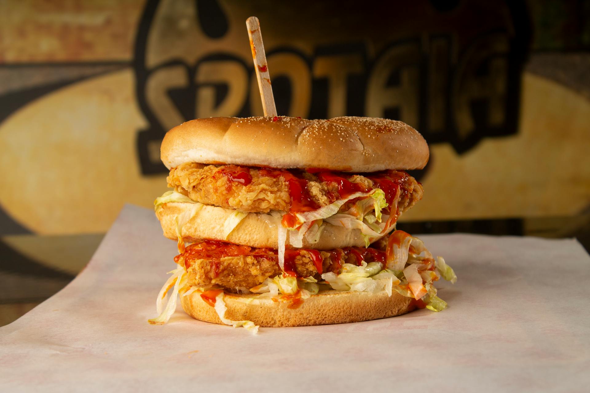 Mouth-watering double stacked fried chicken burger with lettuce and sauce on a table.