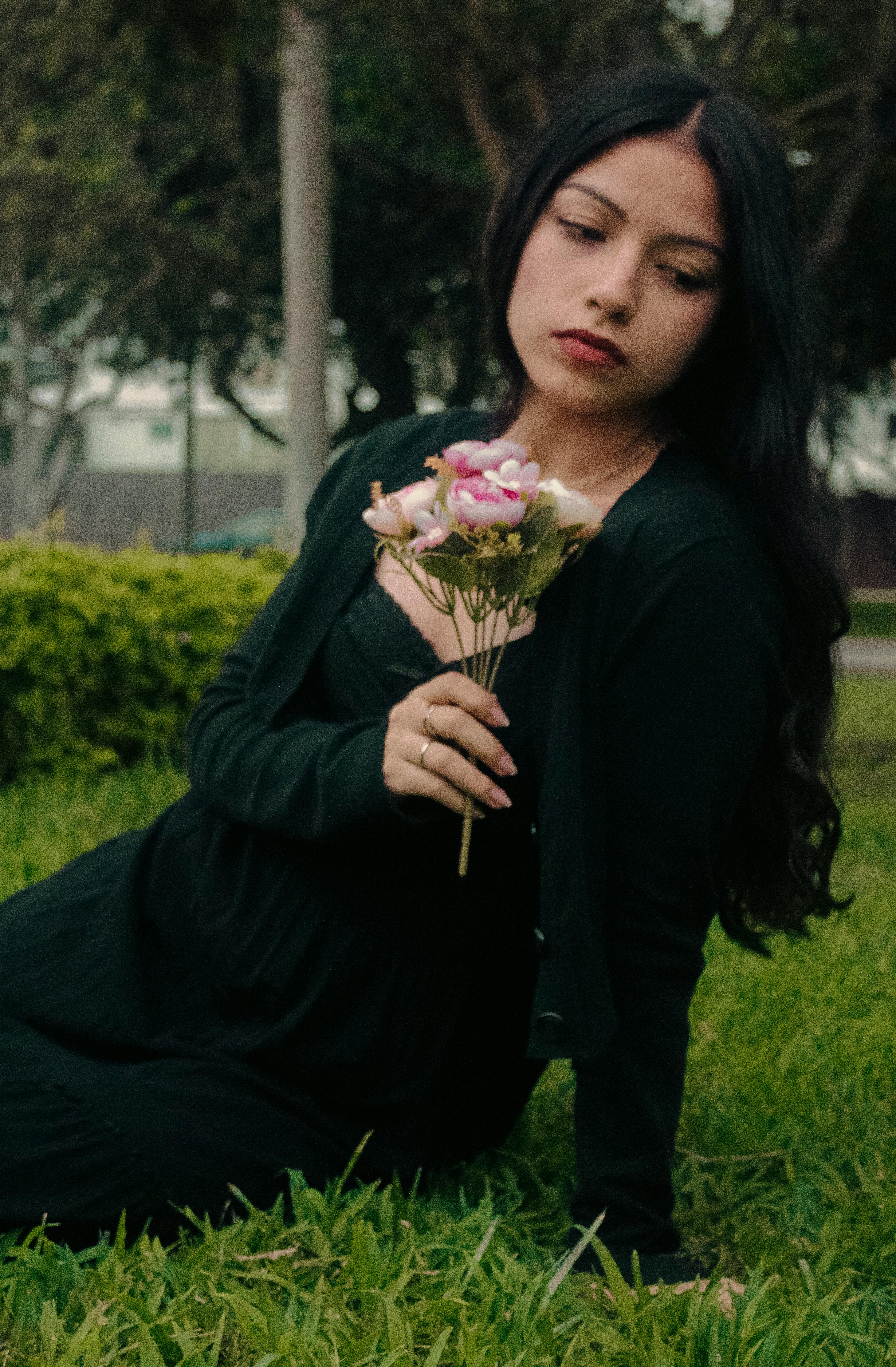 Young woman in black attire holding flowers, sitting on grass in Lima, Peru.