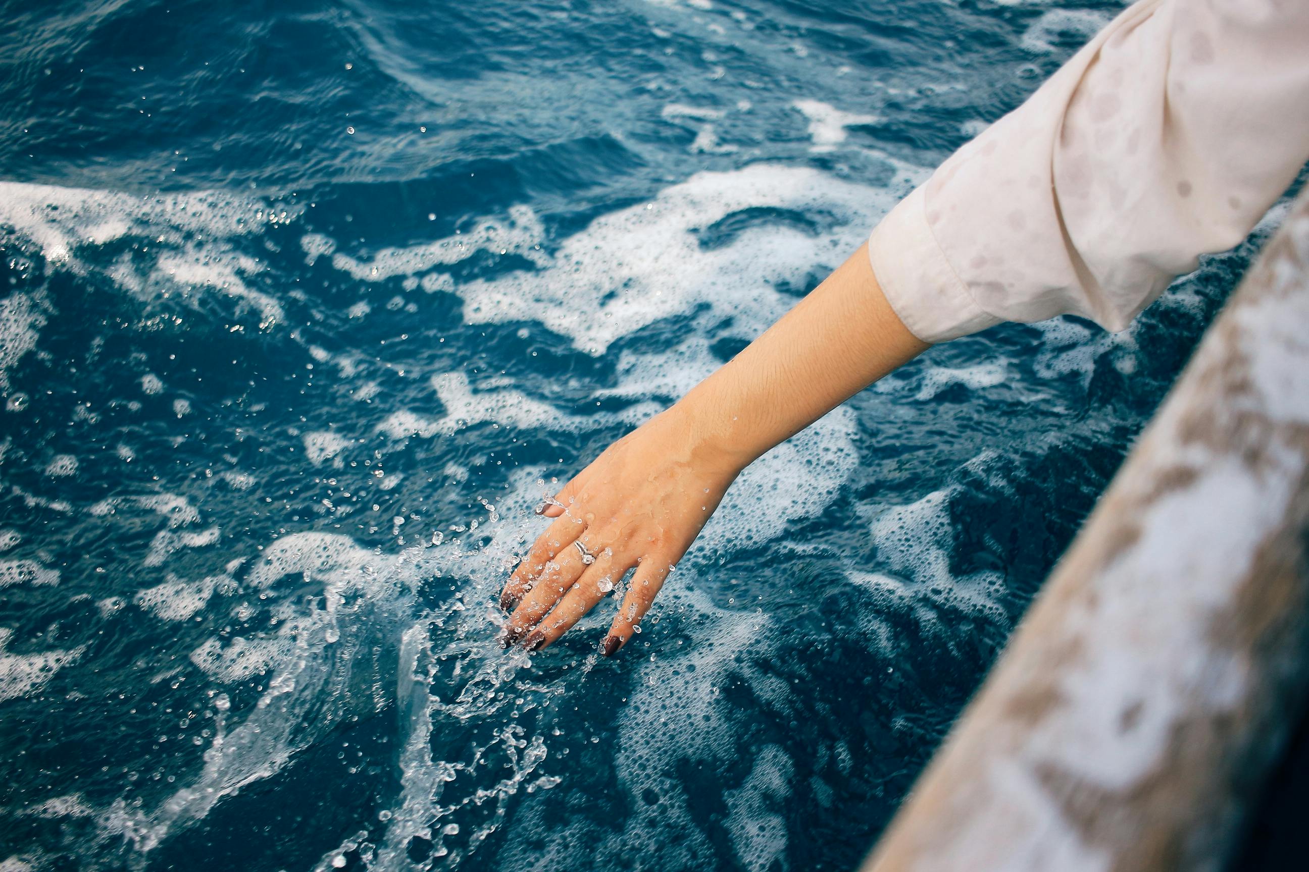 A person's hand gently touching the clear blue ocean water from a boat. Perfect summer scene.