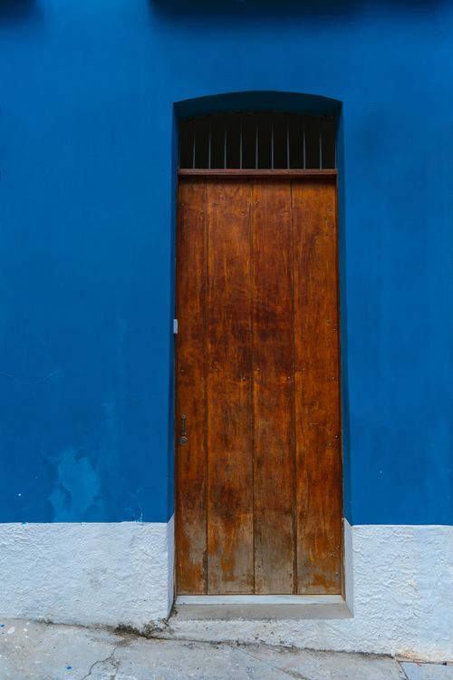 Free Rustic wooden door set in a striking blue wall, perfect for urban architectural themes. Stock Photo