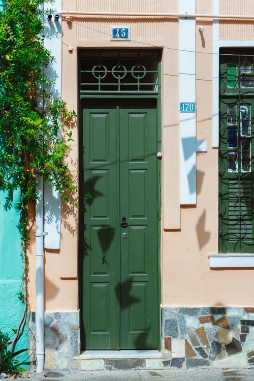 Free Explore the charm of a green door on a vibrant urban street, framed by colorful walls and lush greenery. Stock Photo
