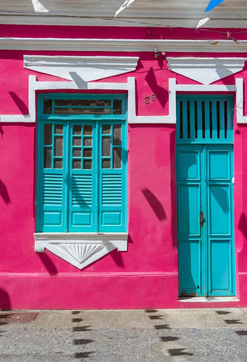 Free A vibrant pink facade featuring turquoise shutters and door on a sunny day. Stock Photo