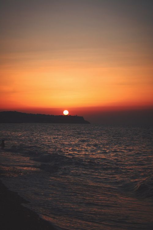 Free Stunning sunset over the ocean with a clear sky and waves lapping at the shore. Stock Photo