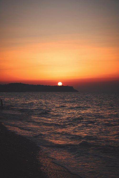 Free Beautiful sunset over the ocean with gentle waves lapping at the shore, creating a serene and picturesque scene. Stock Photo