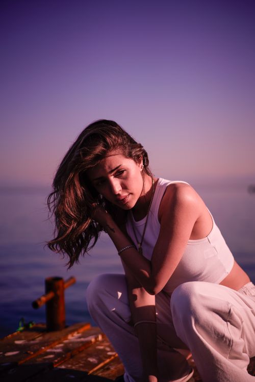 Free A woman in sportswear poses contemplatively on a pier at sunset, exuding serenity and style. Stock Photo