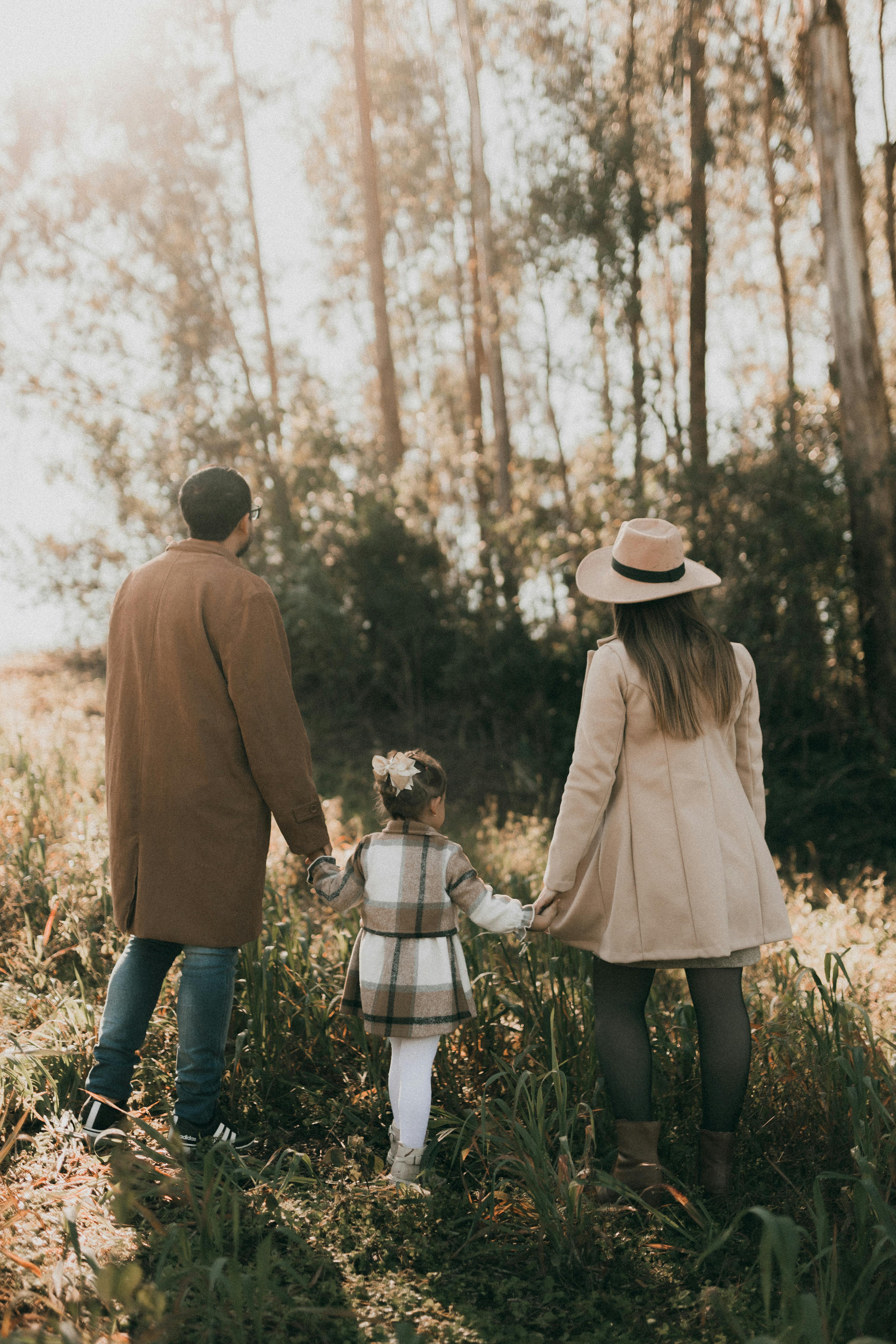 Family of three enjoying a walk in a sunlit forest, holding hands.