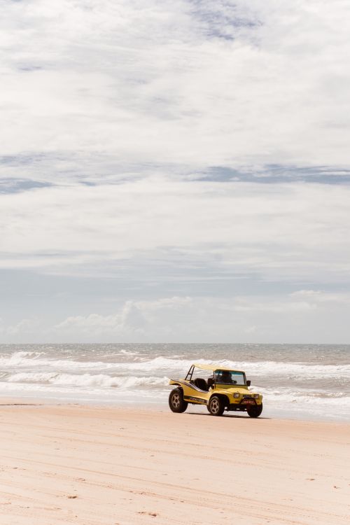 Free Yellow buggy on sandy beach with waves under a cloudy sky. Perfect for summer travel adventures. Stock Photo