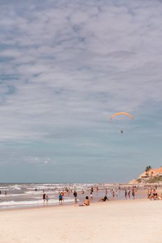 Vibrant beach scene with people enjoying the summer sun while a paraglider soars above.