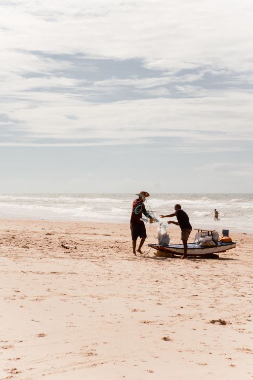 Free Two fishermen prepare their boat on a sunny beach, capturing the essence of coastal life. Stock Photo