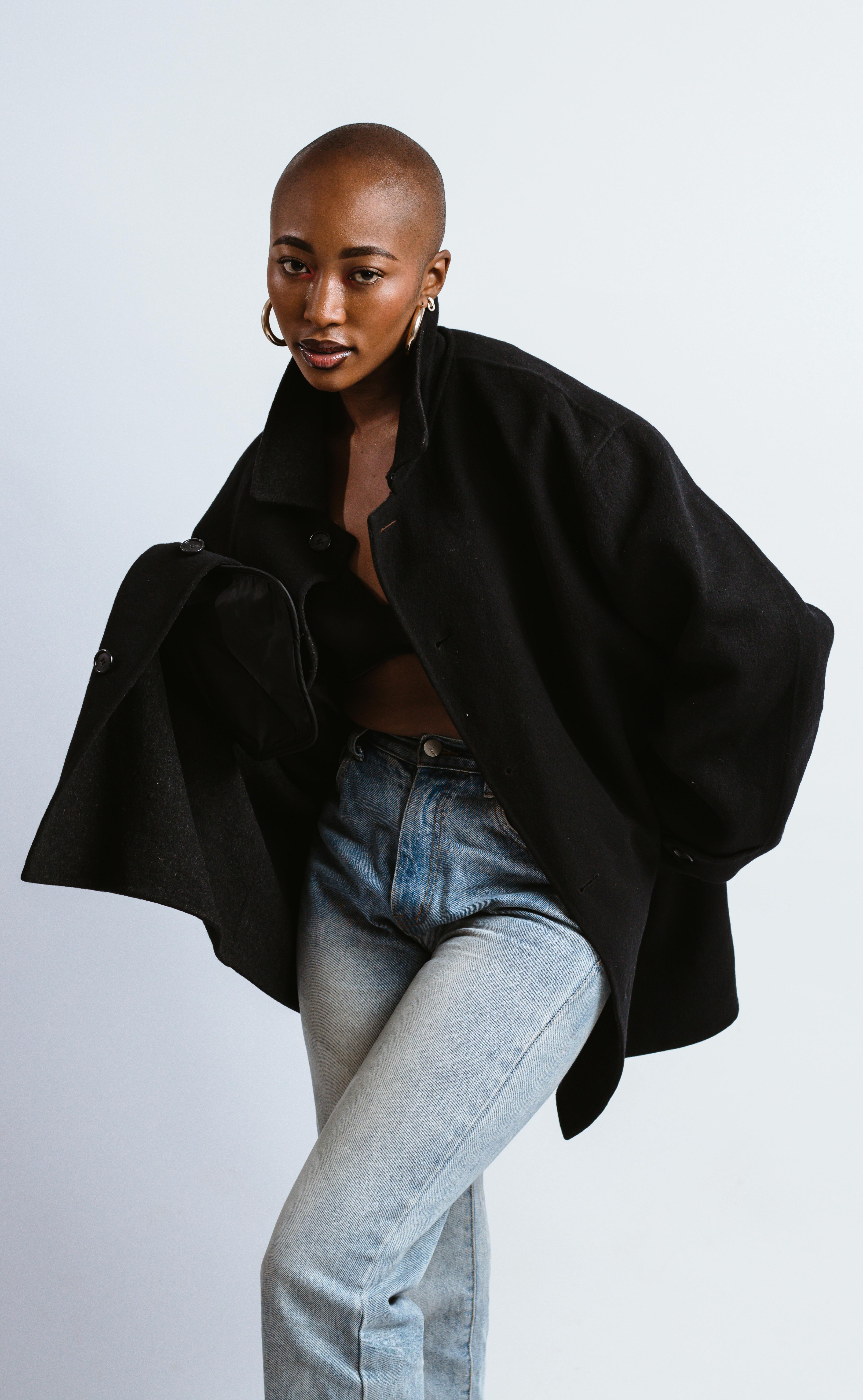 Elegant portrait of a woman posing in a studio, showcasing modern fashion with a black coat and jeans.