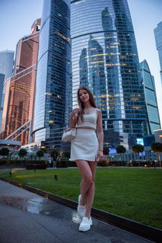 Young woman posing in a modern cityscape with glass skyscrapers.