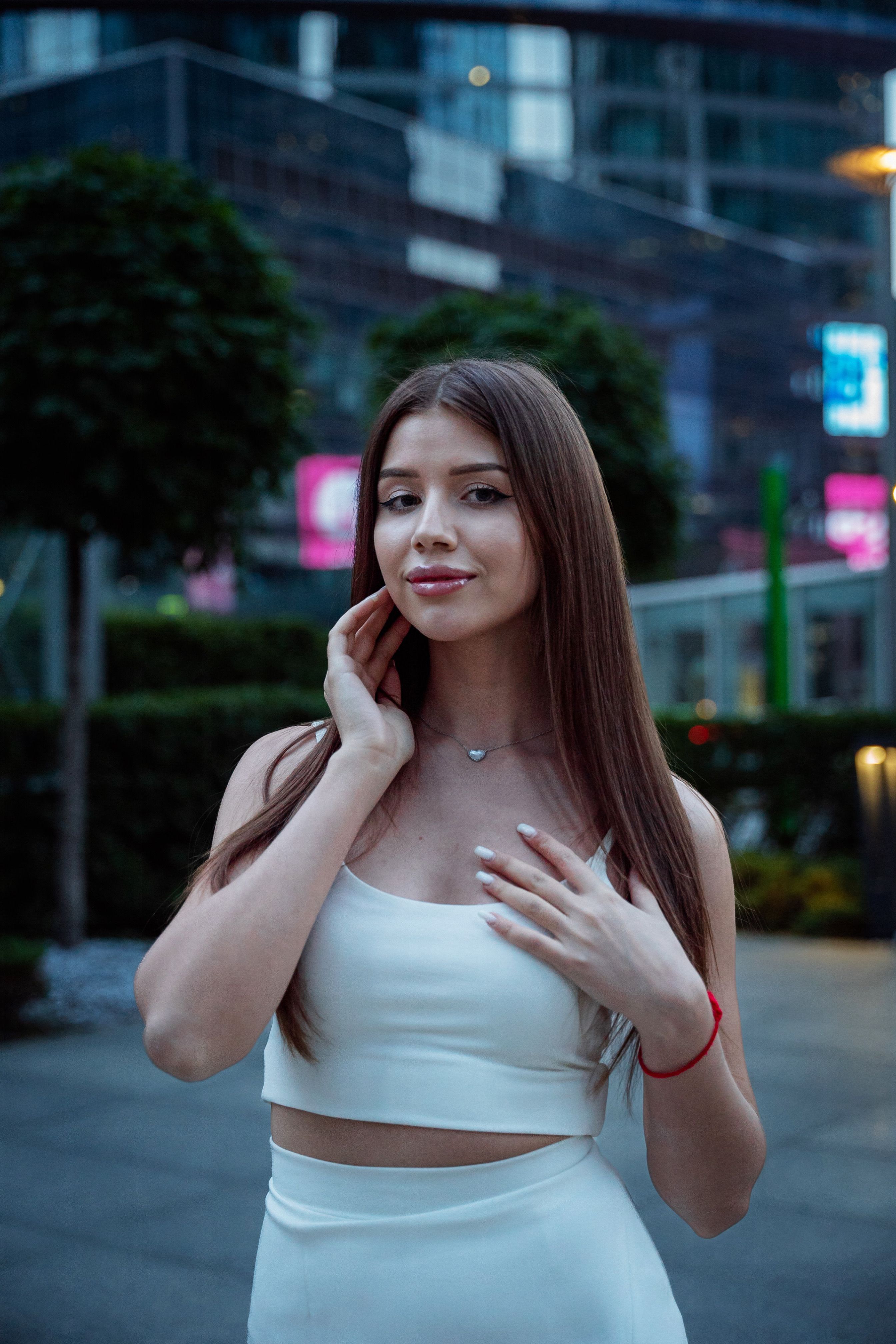 Stylish young woman in urban setting with long brown hair wearing a white top.