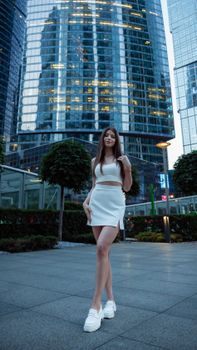 Young woman in white outfit posing downtown with skyscrapers in the background.