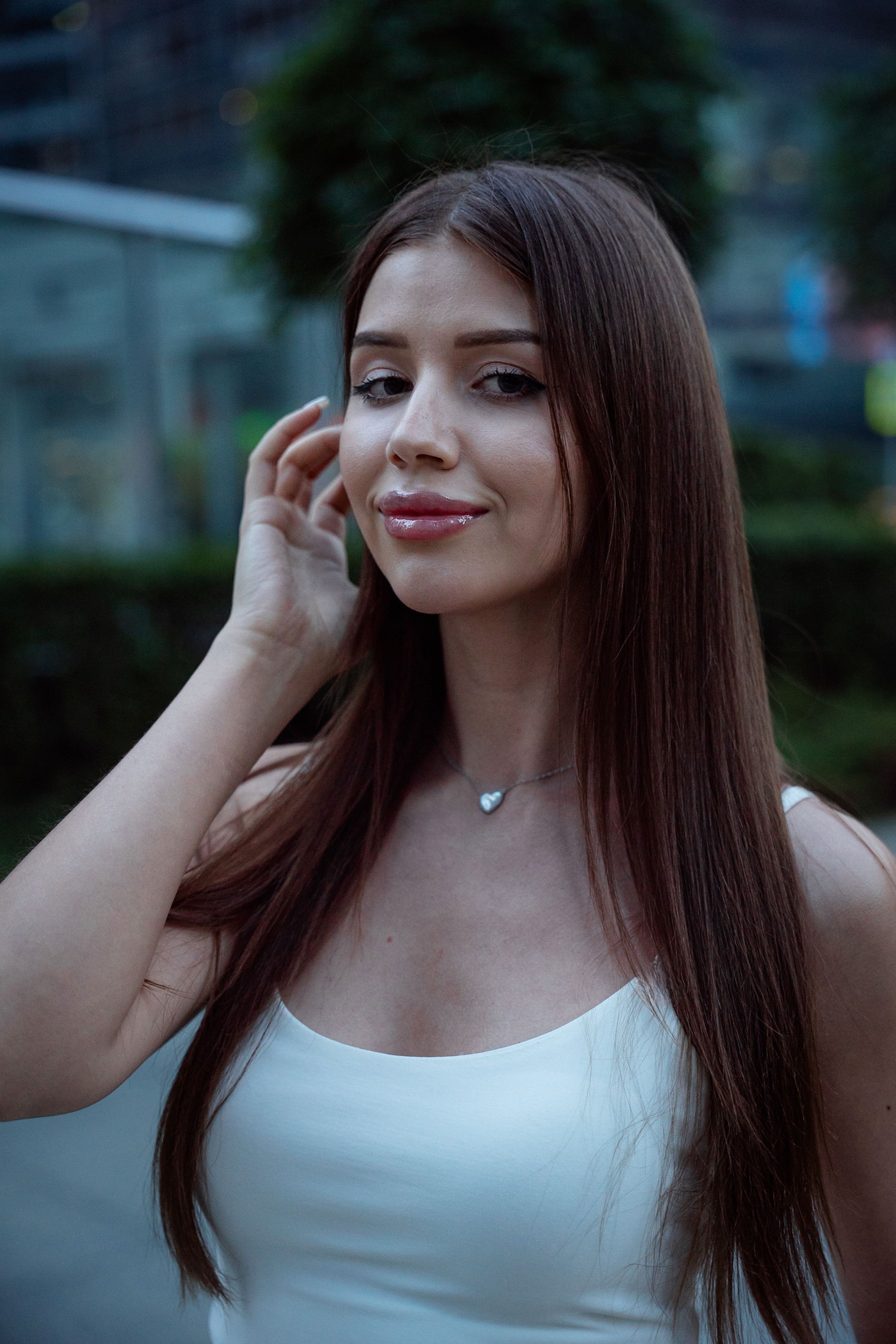 Portrait of a fashionable woman with long brown hair, posing outdoors in an urban environment.