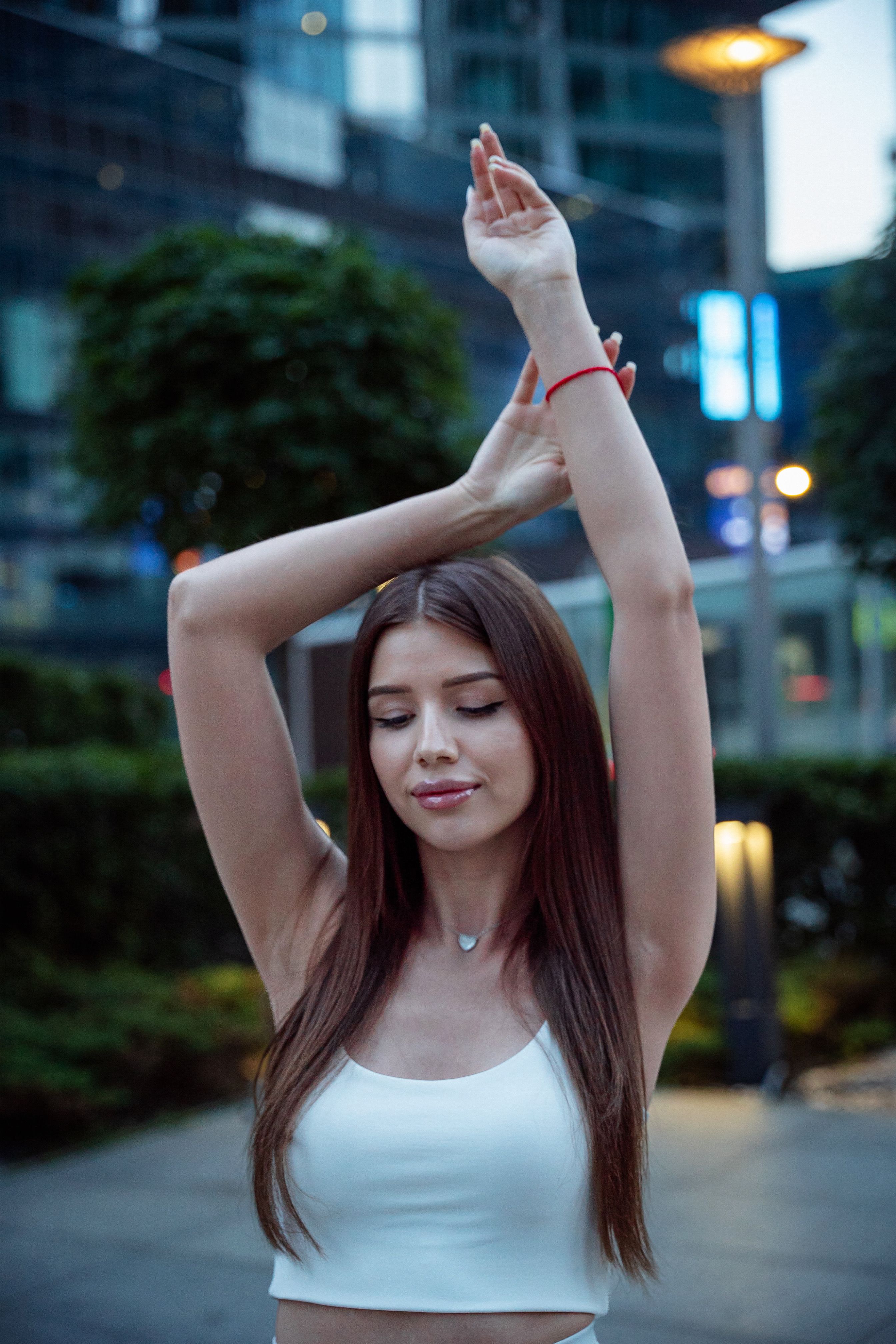 Brunette woman stands peacefully in a city environment at dusk, embodying tranquility.