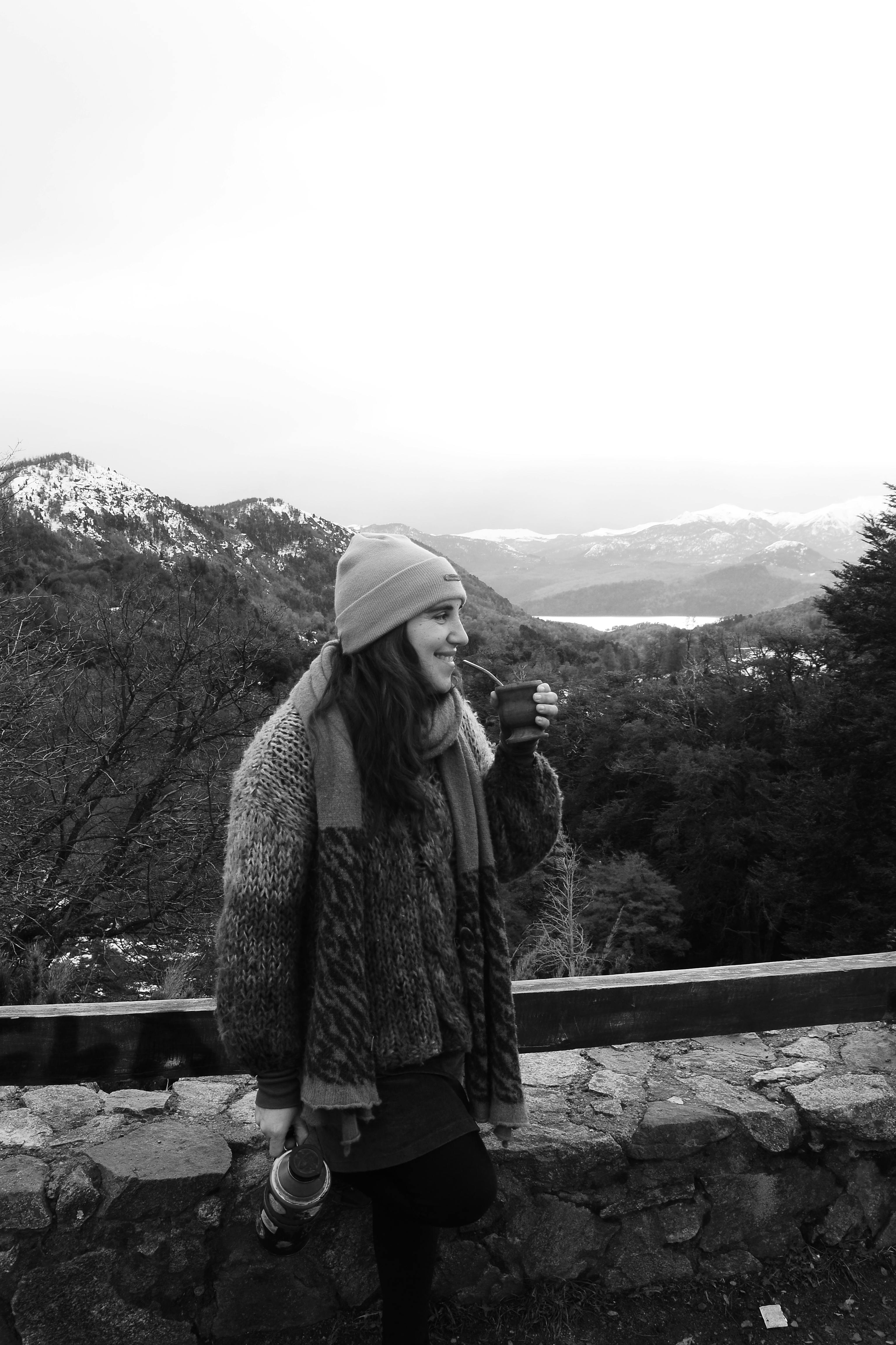 Woman in winter attire enjoying a hot drink with a mountain backdrop.