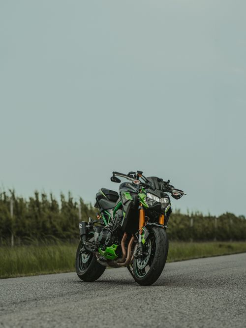 Free A green motorcycle parked on an open road surrounded by nature, perfect for travel enthusiasts. Stock Photo