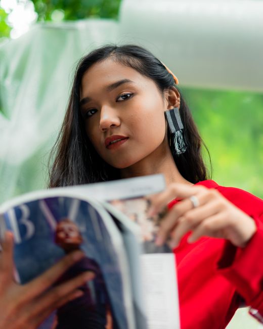 Portrait of a woman in a red outfit elegantly reading a magazine.