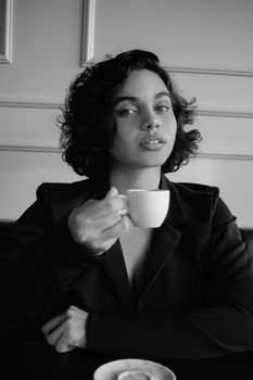 Elegant woman in black and white holding a cup, showcasing modern fashion style.
