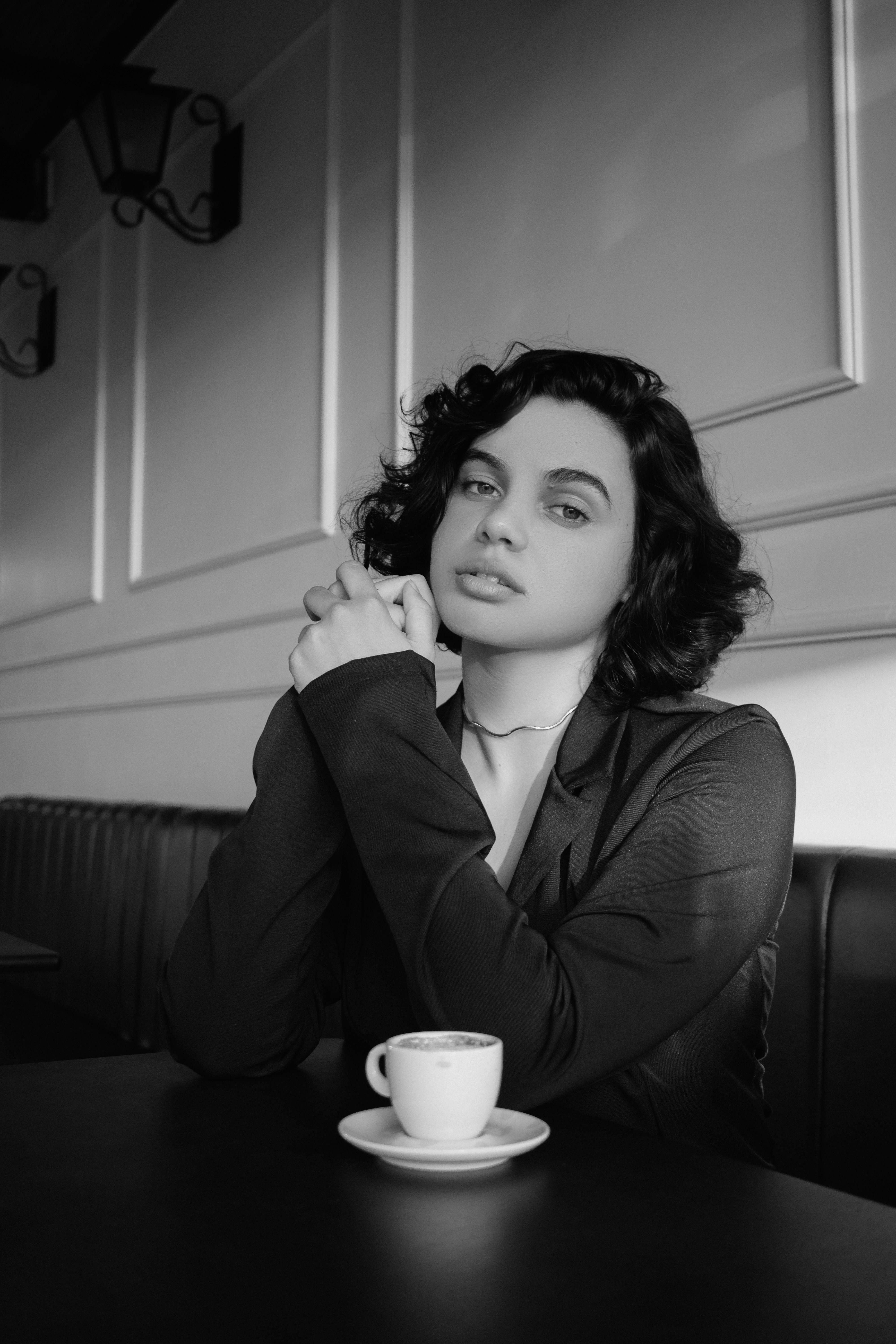 Black and white photo of a woman sitting in a café, with a coffee cup on the table.