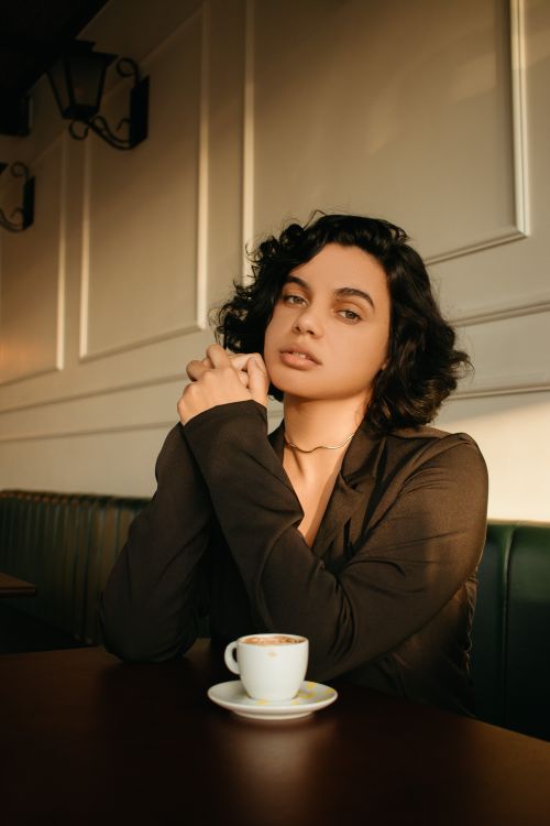 Free Stylish woman seated in a café, enjoying a coffee under warm lighting. Stock Photo