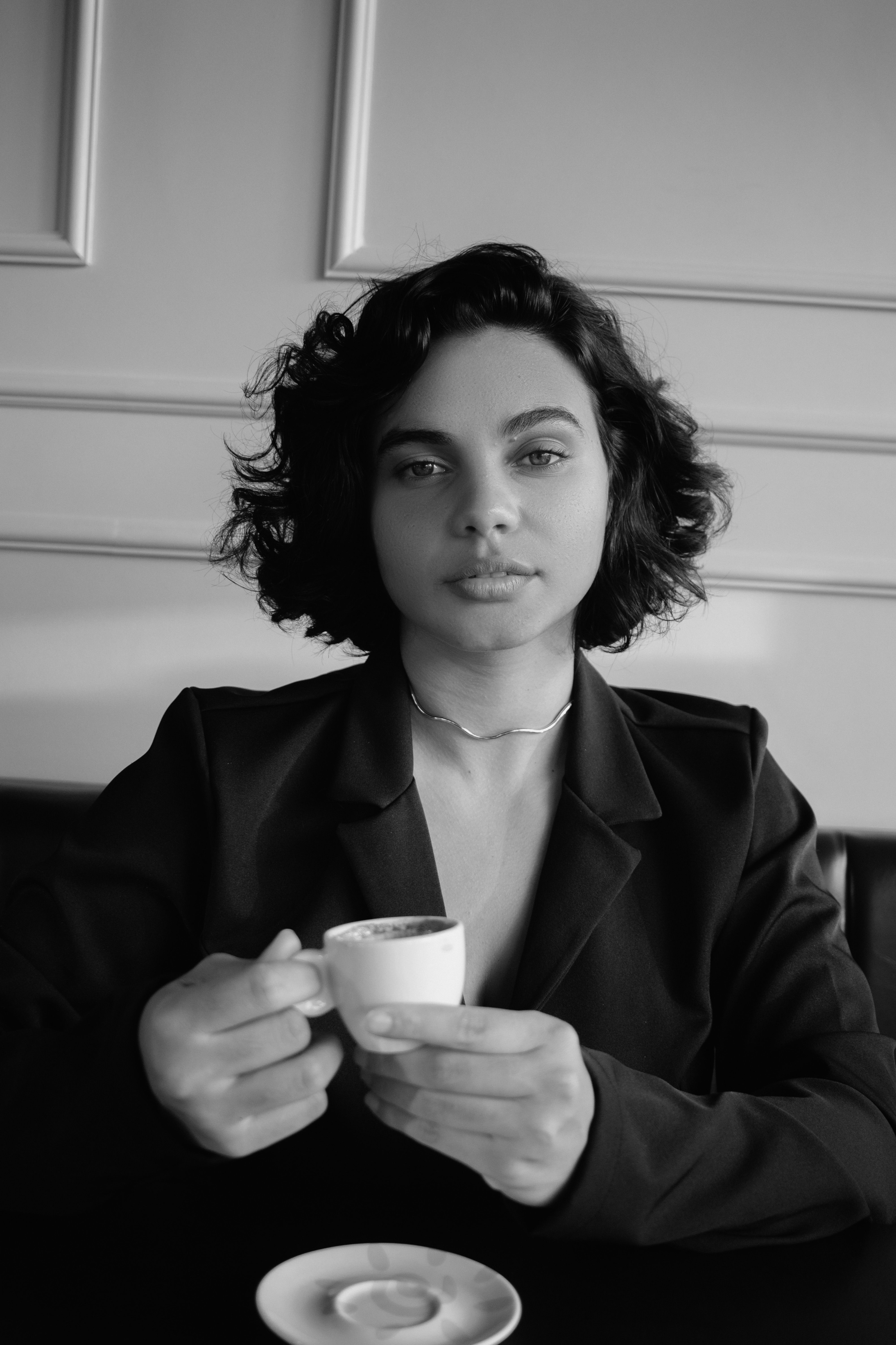 Black and white portrait of an elegant woman holding a coffee cup in a stylish café.