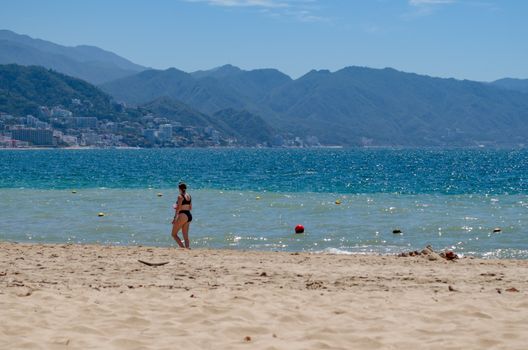 Woman walking on a sandy beach in Puerto Vallarta with scenic mountain backdrop.