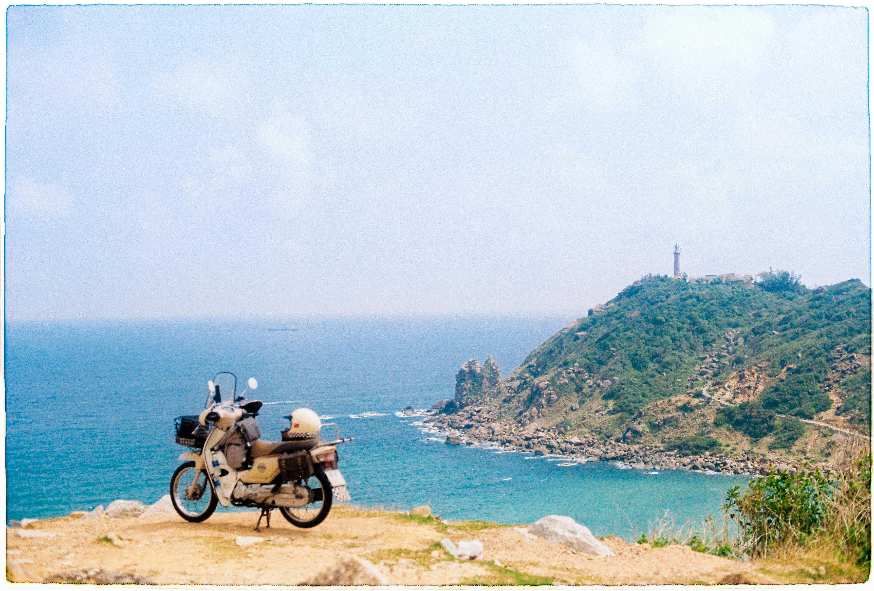 Explore the stunning coastal landscape of Phú Yên, Vietnam with a scenic view featuring a parked motorcycle and a distant lighthouse.